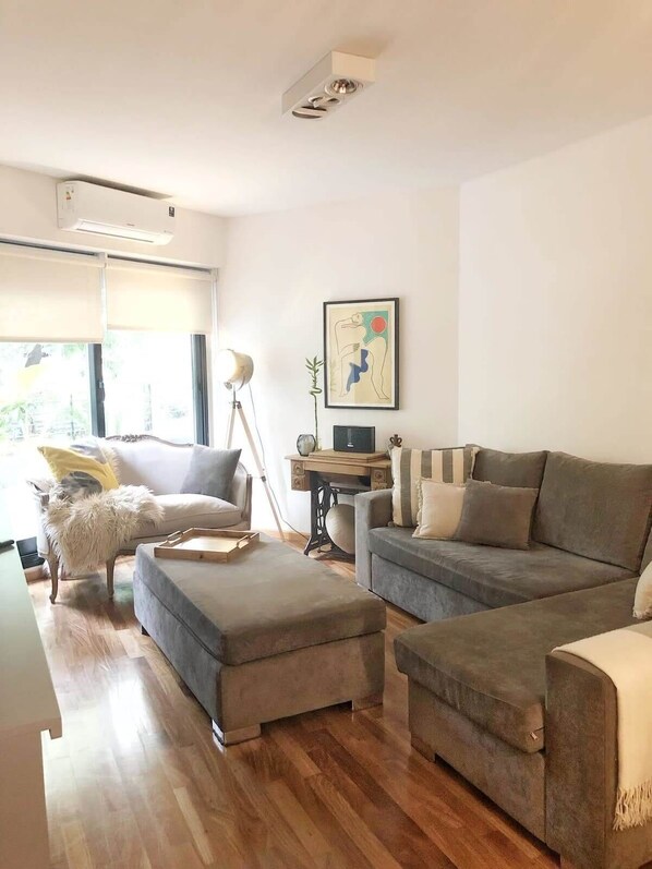 Un salon moderne avec un canapé gris, un pouf et un bureau avec une lampe.