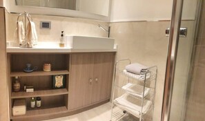 Une salle de bain équipée d’un lavabo, d’étagères pour les articles de toilette, d’un porte-serviettes et d’une cabine de douche en verre.
