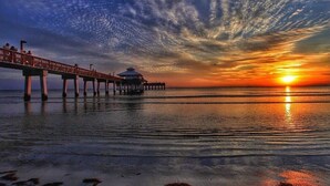 Eine Pier, die sich in ruhiges Wasser bei Sonnenuntergang erstreckt, bewölkter Himmel.