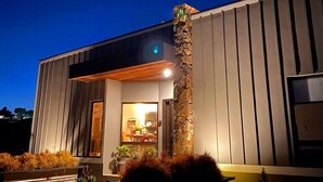 A modern building with a stone column, a large glass door, and a well-lit interior. - BEAUTIFULL VINEYARD HOUSE (CASA MAZAHUA)  IN VALLE DE GUADALUPE (VALLE DE GUADALUPE)