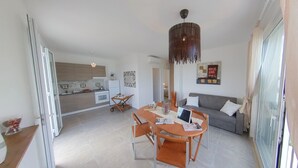 Una sala de estar moderna con un sofá gris, una mesa de comedor con sillas, una computadora portátil y una lámpara colgante.