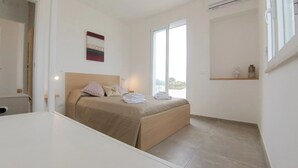 Un dormitorio con una cama, una mesita de noche, una ventana y una obra de arte colgada en la pared.