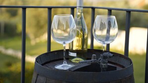 Dos copas de vino sobre un barril, junto a una botella y un grifo, con un fondo exterior desenfocado.
