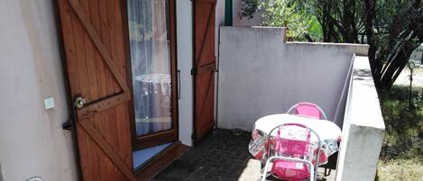 Eine kleine Terrasse im Freien mit Tisch und Stühlen, einer Holztür und einer Betonmauer.