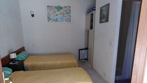 A room with two beds, a nightstand, a small table, a painting on the wall, and a bathroom door.