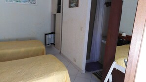 A room with two beds, a small cabinet, a painting, and a shower area.