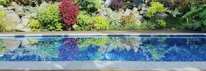 A swimming pool with a stone wall and various plants in the background. - Rainbow Villas (Rarotonga)