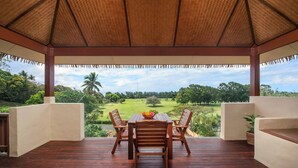 A covered outdoor seating area with a table and chairs, overlooking a lush landscape. - Rainbow Villas (Rarotonga)