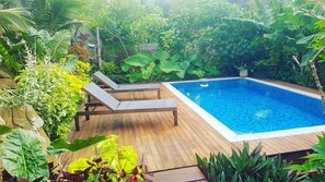 A wooden deck with a rectangular pool surrounded by lush greenery and a few lounge chairs. - Rainbow Villas (Rarotonga)