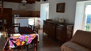 A cozy kitchen with a dining table covered in a colorful tablecloth, wooden cabinets, and a hanging light fixture. - Gîte in the heart of the Lozère Cévennes (La Falguière)
