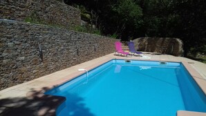 Una piscina con un muro de piedra y algunas sillas de descanso.