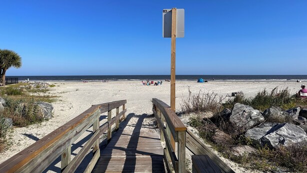 Un muelle de madera que conduce a una playa, bajo un cielo azul despejado.