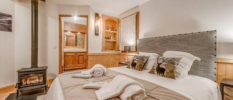 Un dormitorio con una cama grande, cabecera de madera, mesita de noche, lámpara, espejo, armario de madera y estufa de leña.