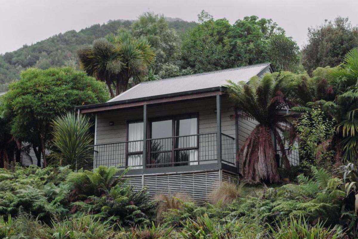 A small, single-story house surrounded by dense vegetation and trees.
