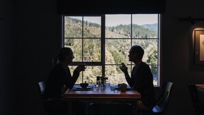 Two people seated at a table with a view of a forest through a window. - Maruia River Retreat (Shenandoah)