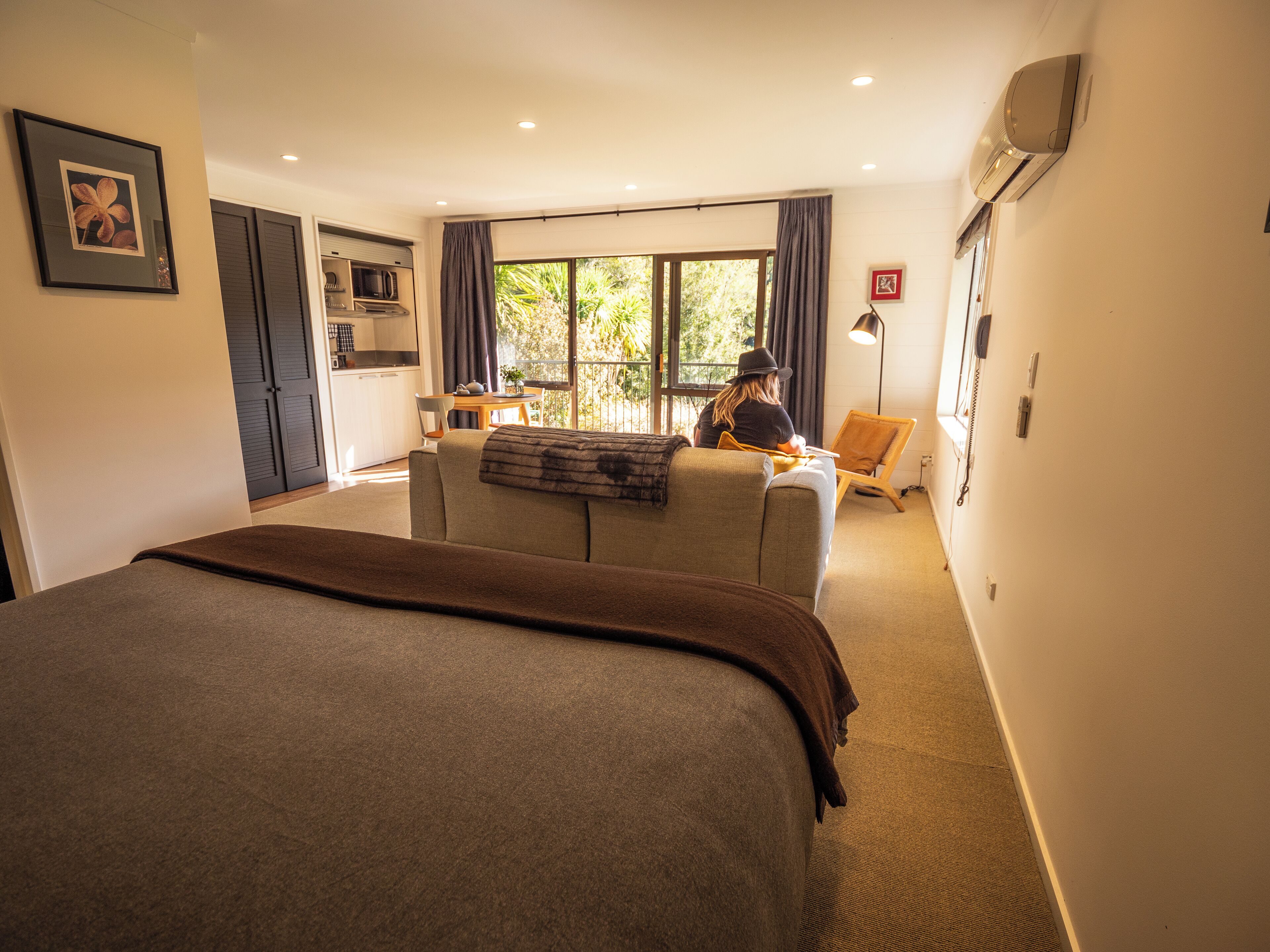 A bedroom with a large bed, a sofa, a desk, and a view of the outdoors.
