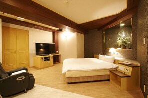 A hotel room with a bed, a TV, a massage chair, and a wooden wardrobe. - Hotel NOA - Adults Only (Anjo)