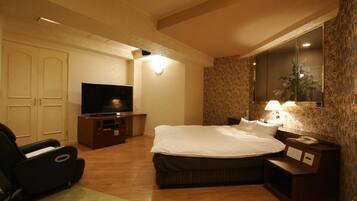 Habitación de hotel con cama, televisor, sillón de masaje y escritorio con lámpara.