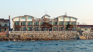 A waterfront hotel with multiple balconies, outdoor umbrellas, and a stone wall. - Marronnier Pension (Taean)