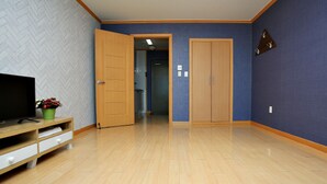 A room with a television on a wooden stand, a potted plant, and a hallway leading to a wardrobe. - Marronnier Pension (Taean)