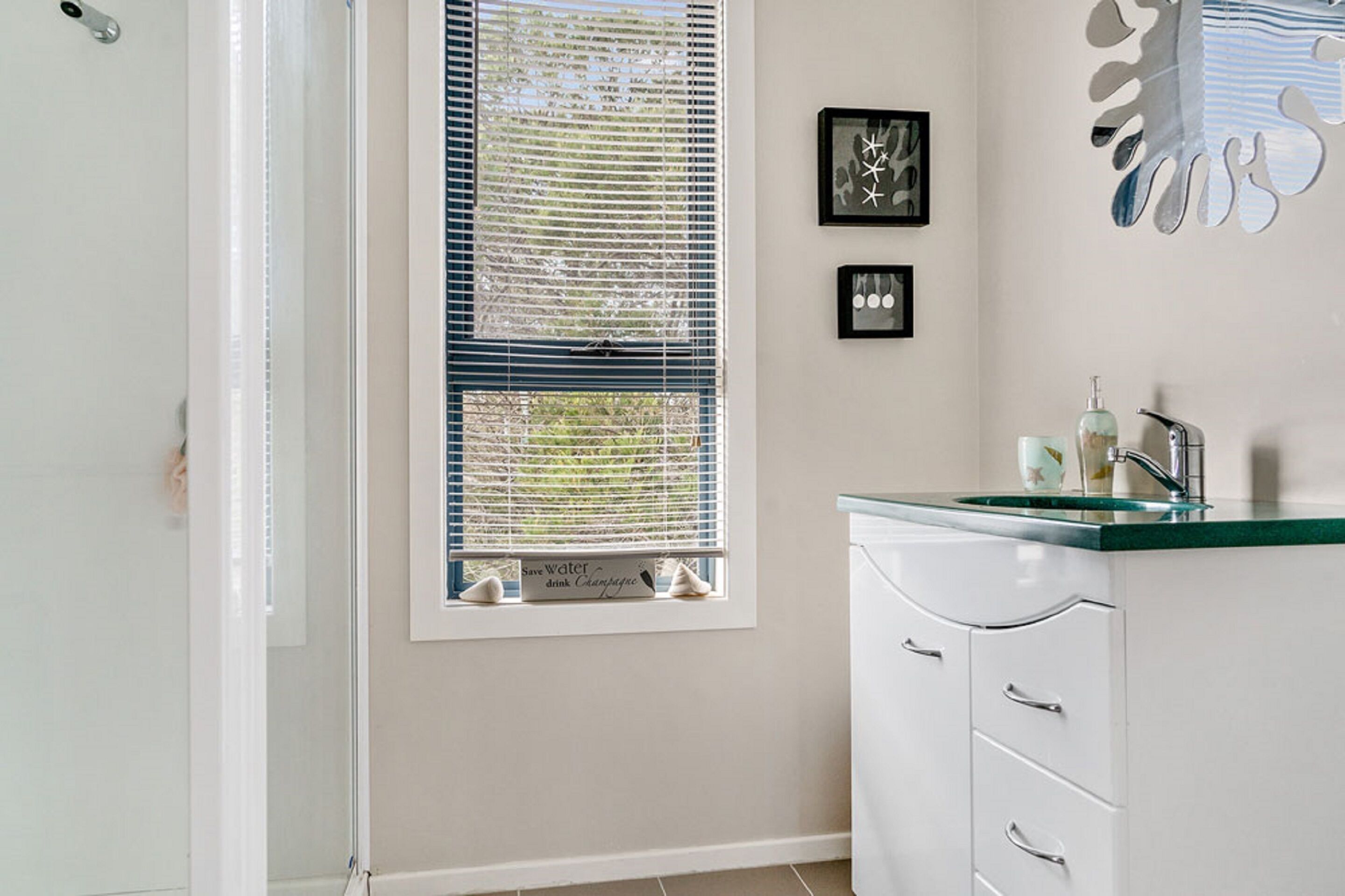 A bathroom with a shower, a sink with a green countertop, and a window with blinds.