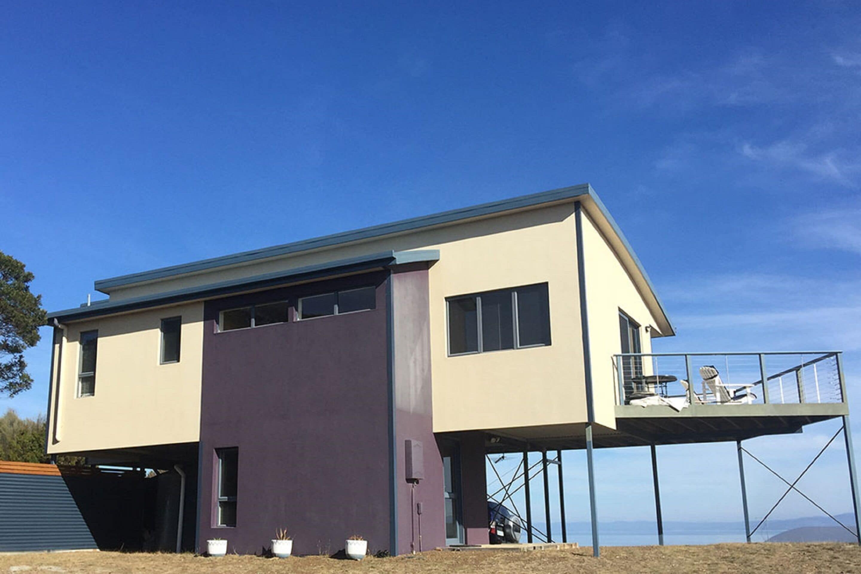 A modern two-story house with a flat roof, a balcony on the upper floor, and a garage on the lower level.