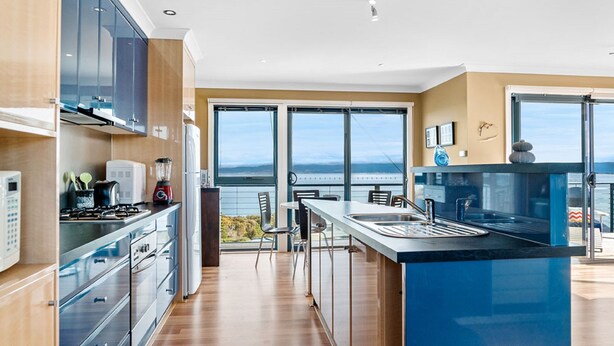 A modern kitchen with large windows, a central island, and a view of the ocean. - Freycinet Dream (Coles Bay)