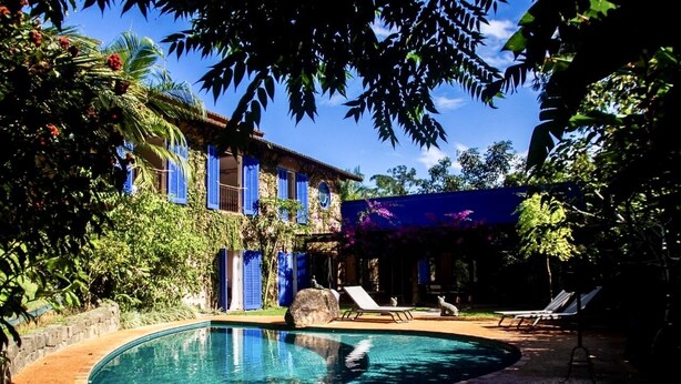 A swimming pool with lounge chairs, a house with blue shutters, and lush greenery. - Beautiful house in Ilhabela (Ilhabela)