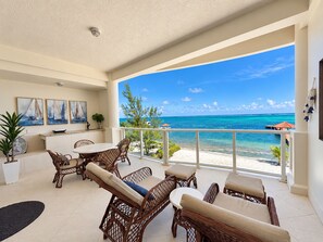 A balcony with wicker furniture, a dining table, and a view of the ocean.