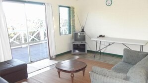 A living room with a sofa, a coffee table, a TV on a stand, a dining table, and a window with curtains. - Green Lodge Holiday Homes (Nuku'alofa)