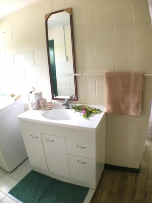 A bathroom with a white sink, a mirror, a towel, and a green rug. - Green Lodge Holiday Homes (Nuku'alofa)