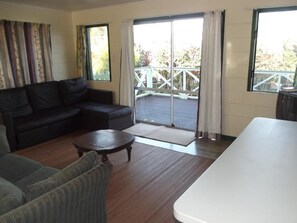 Ein Wohnzimmer mit einer Couch, einem Sessel und einem Couchtisch. Ein Glastür führt auf einen Balkon mit Geländer.