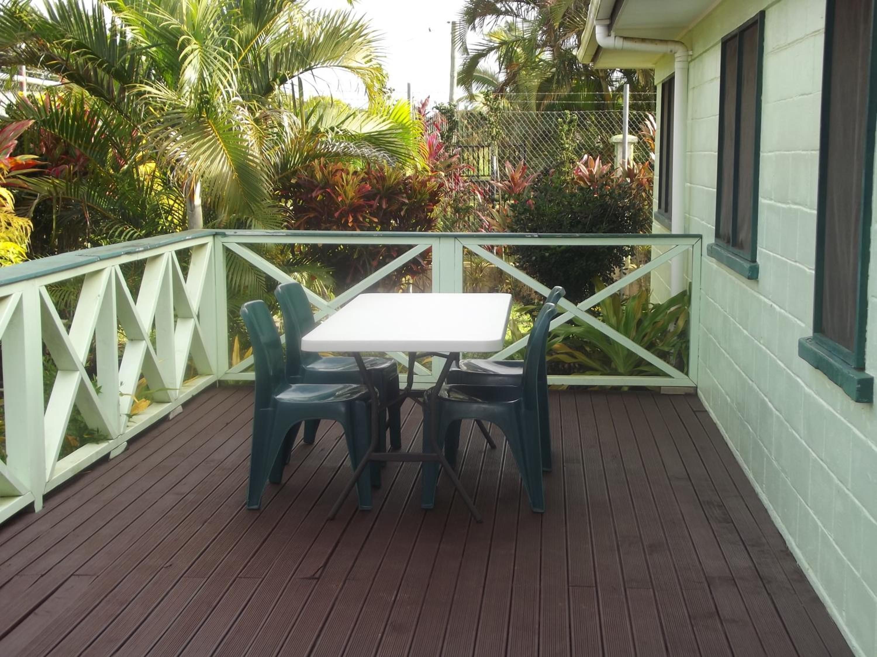 A covered outdoor area with a table and chairs, surrounded by a railing and lush greenery.