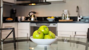 A bowl of green apples on a glass table in a kitchen with white cabinets and a microwave.