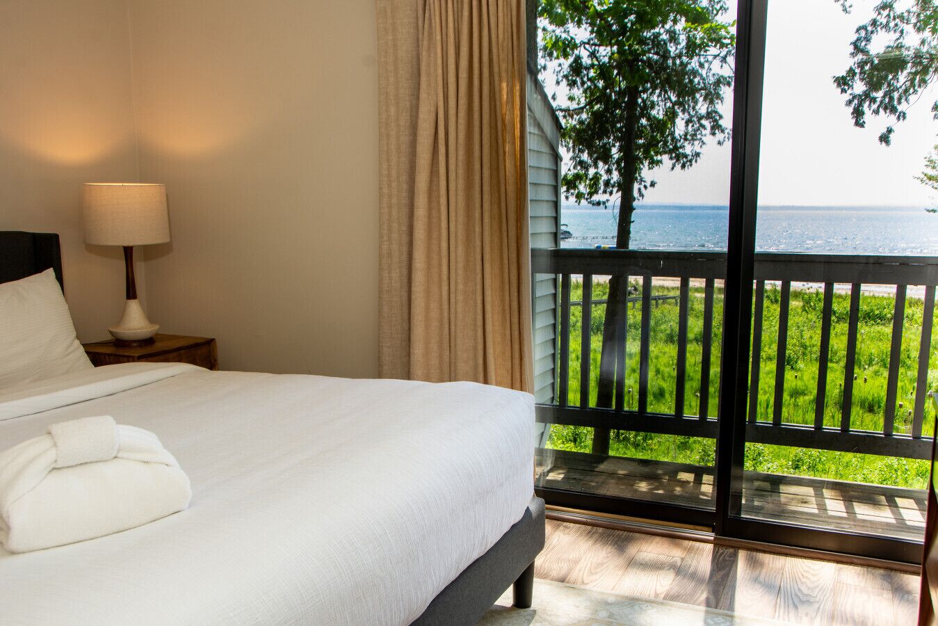Habitación de hotel con cama, mesita de noche con lámpara y vista al mar a través de grandes ventanales.