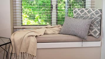 Ein Fensterplatz mit einer beige farbenen Decke, einem grauen Kissen und einem gemusterten Kissen.