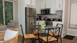 A modern kitchen with white cabinets, stainless steel appliances, and a glass dining table with wicker chairs.