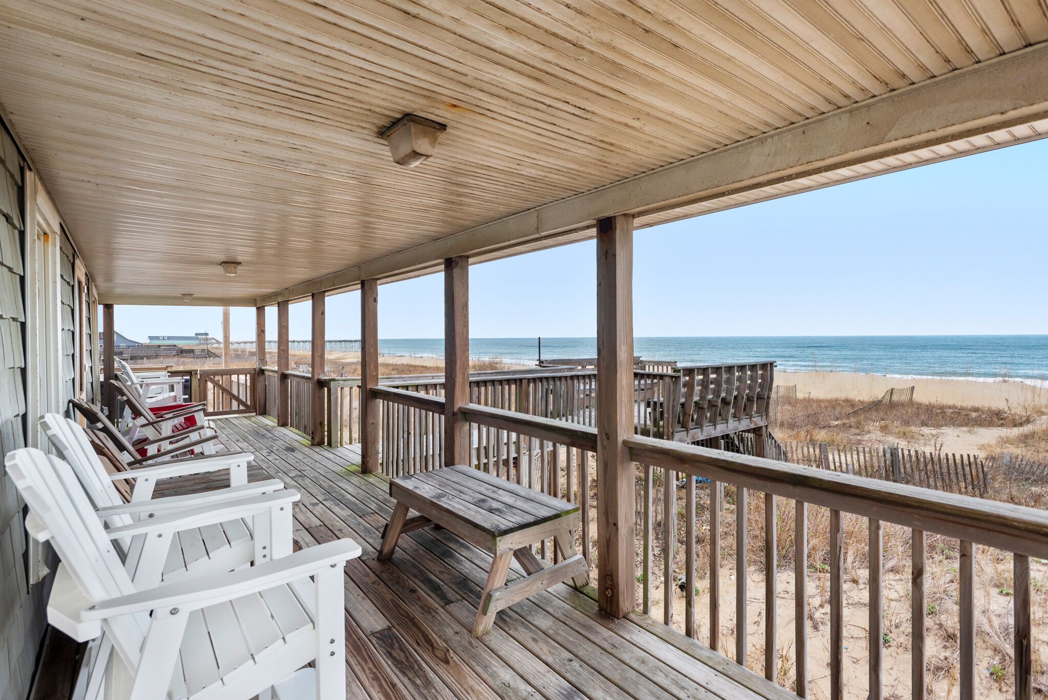 A wooden deck with white Adirondack chairs and a picnic table, overlooking a beach.