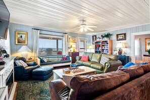 A living room with a large window, a ceiling fan, a bookshelf, and a chessboard on the coffee table.