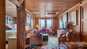 Interior acogedor de una cabaña con techo de madera, un sofá, una silla, una mesita y una alfombra colorida.