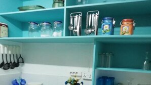 Uma cozinha com armários verde-água, micro-ondas, cafeteira e diversos utensílios de cozinha.