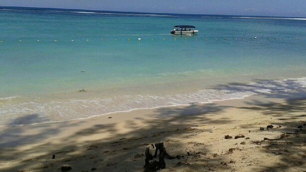Uma praia com águas turquesa cristalinas, um barco e uma costa arenosa.