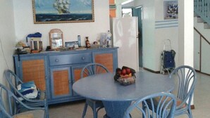 Uma área de refeições com uma mesa redonda, cadeiras azuis e uma cesta de frutas.