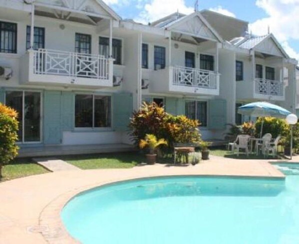 A two-story hotel with a swimming pool, outdoor seating, and a garden area.