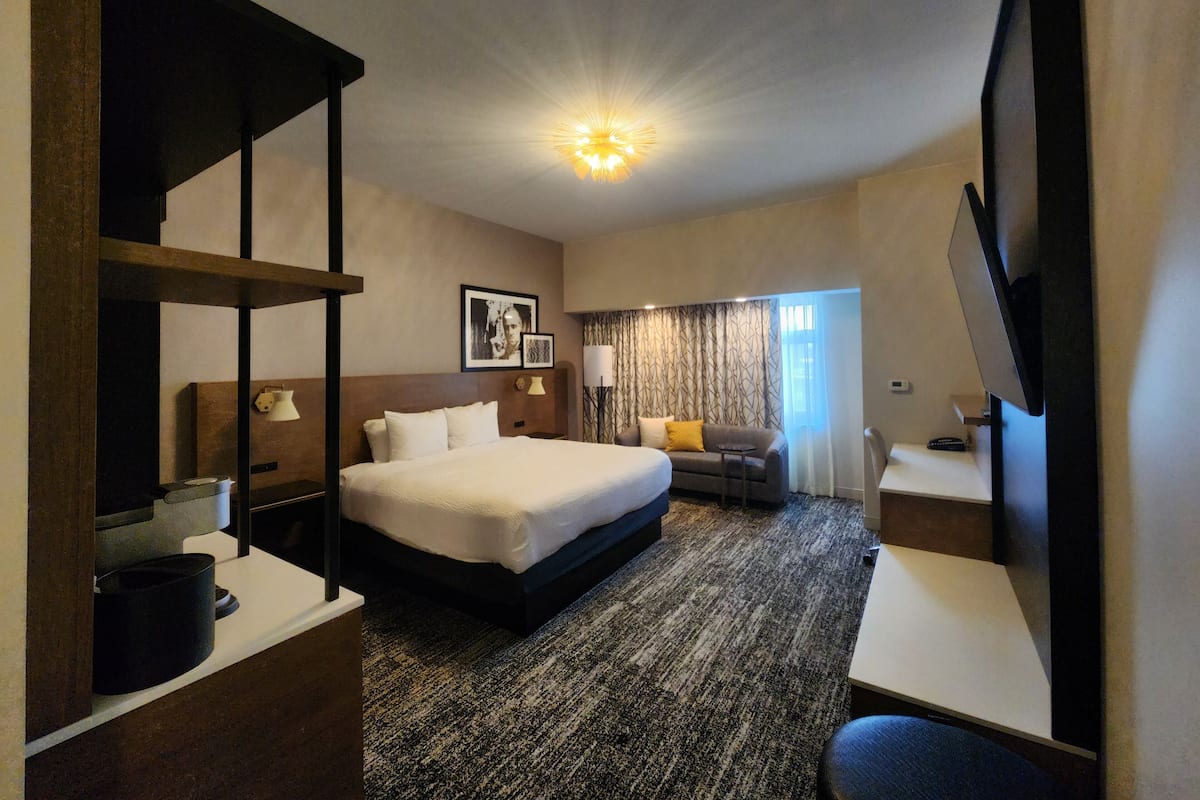 A hotel room with a large bed, a desk, a chair, a television, and a ceiling light.