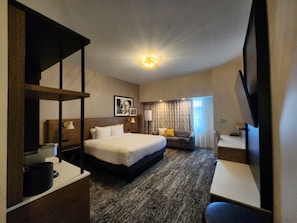 A hotel room with a large bed, a desk, a chair, a television, and a ceiling light. - The Catfish Bend Inn & Spa (Burlington)