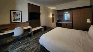A hotel room with a bed, desk, chair, and a TV on the wall. - Great River Hotel (Burlington)