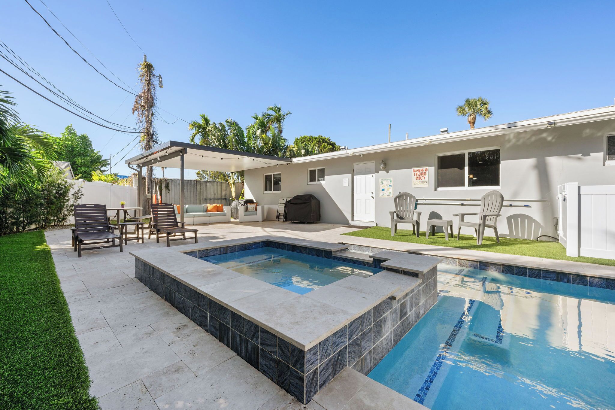 A residential backyard with a swimming pool, patio furniture, and a covered outdoor seating area.