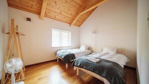 Un dormitorio con dos camas, un ventilador de pie, una ventana y vigas de madera en el techo.