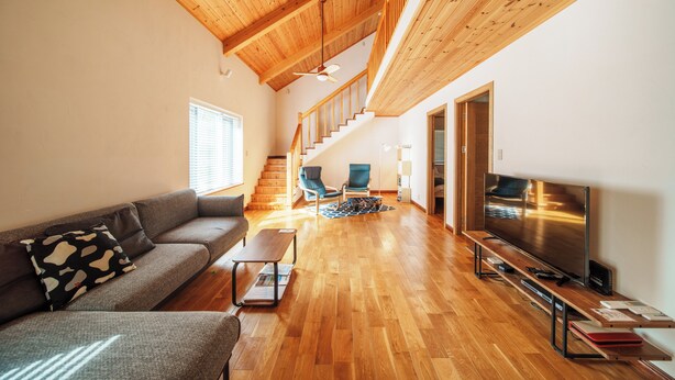 Un salón espacioso con techo de madera, un sofá, un televisor y una escalera que conduce a un nivel superior.